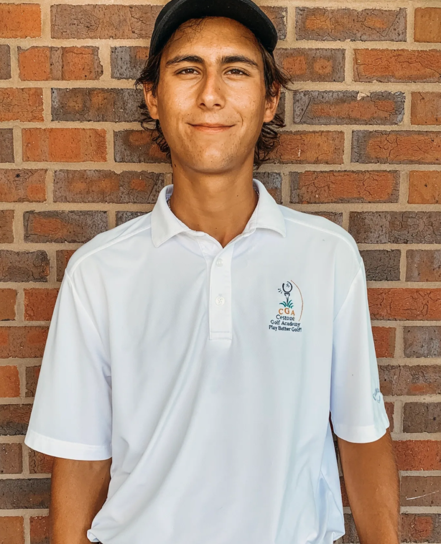 A young man in white shirt standing next to brick wall.